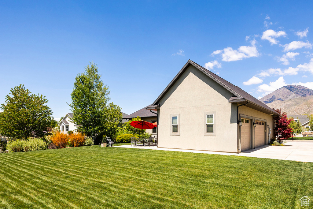 View of home's exterior with a lawn, driveway, a mountain view, an attached garage, and stucco siding