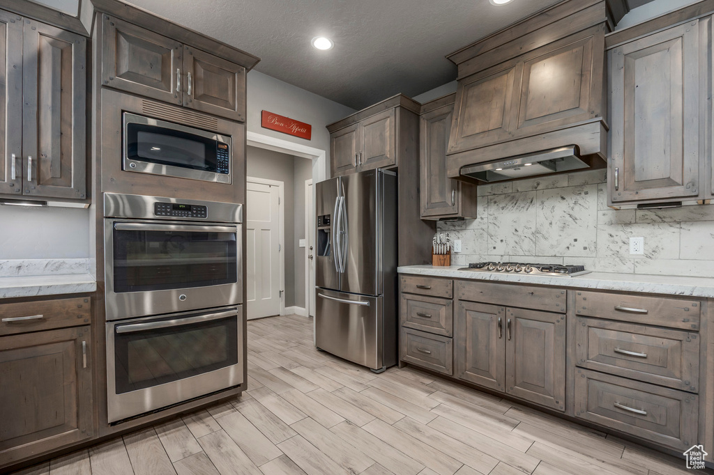 Kitchen with dark brown cabinetry, light wood-type flooring, backsplash, appliances with stainless steel finishes, and recessed lighting