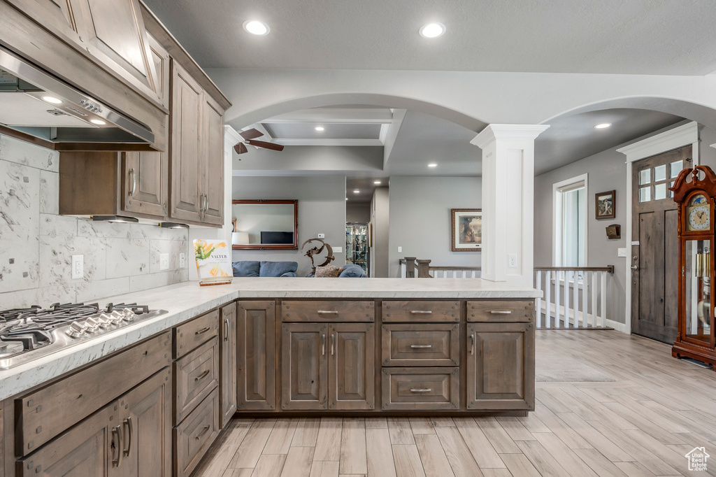 Kitchen with stainless steel gas cooktop, range hood, a peninsula, light countertops, and light wood-type flooring