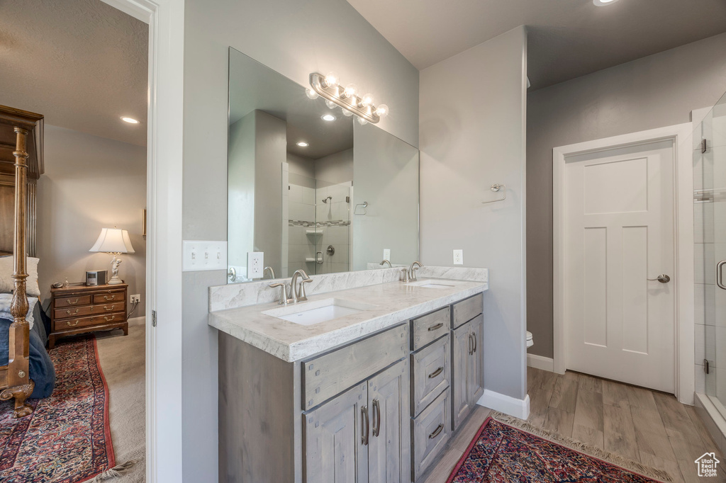 Bathroom with a sink, double vanity, a stall shower, and wood finished floors