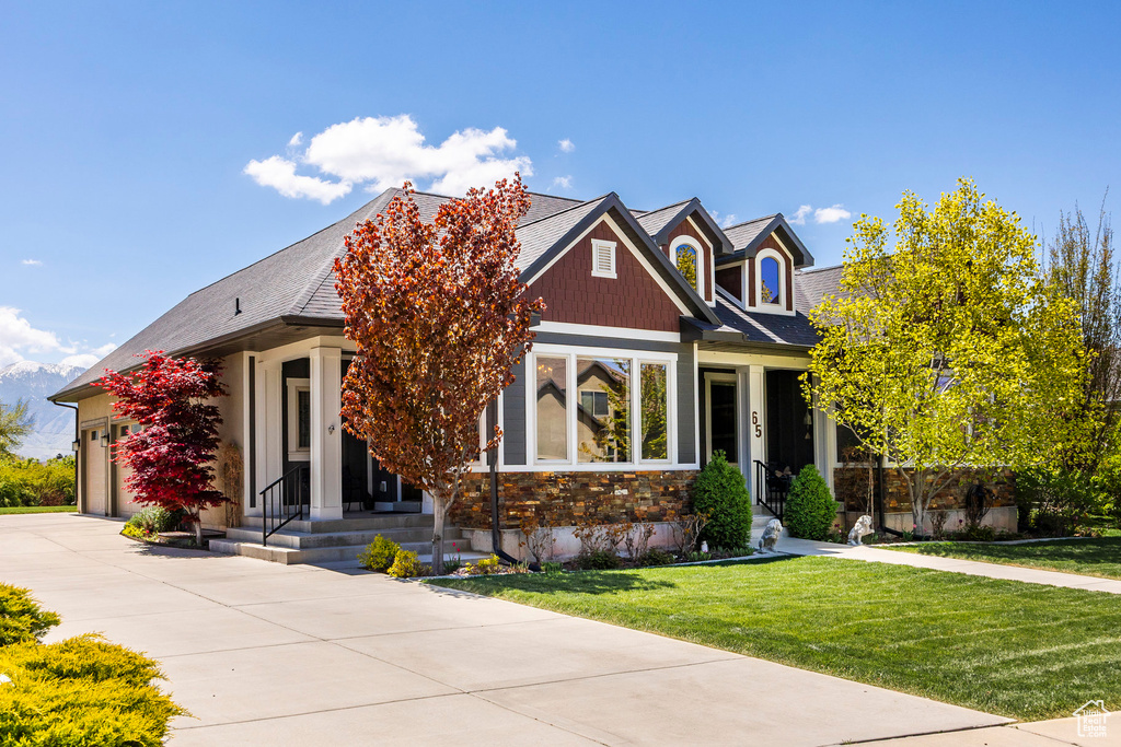 Craftsman inspired home featuring concrete driveway, a garage, stone siding, and a front lawn