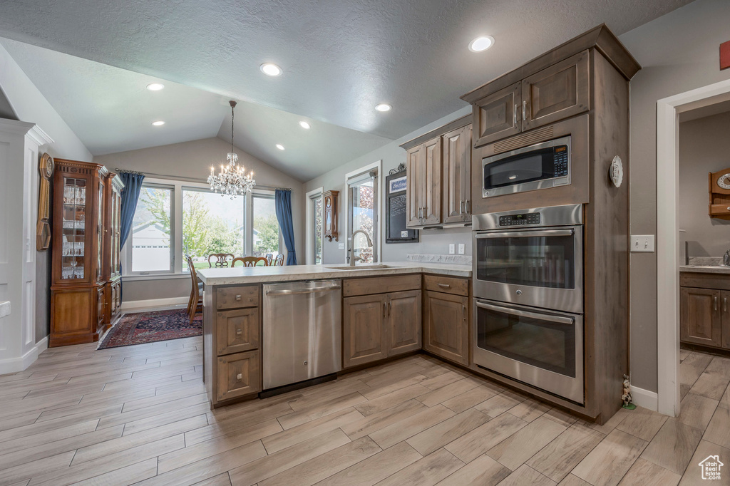 Kitchen featuring a peninsula, an inviting chandelier, a sink, stainless steel appliances, and lofted ceiling
