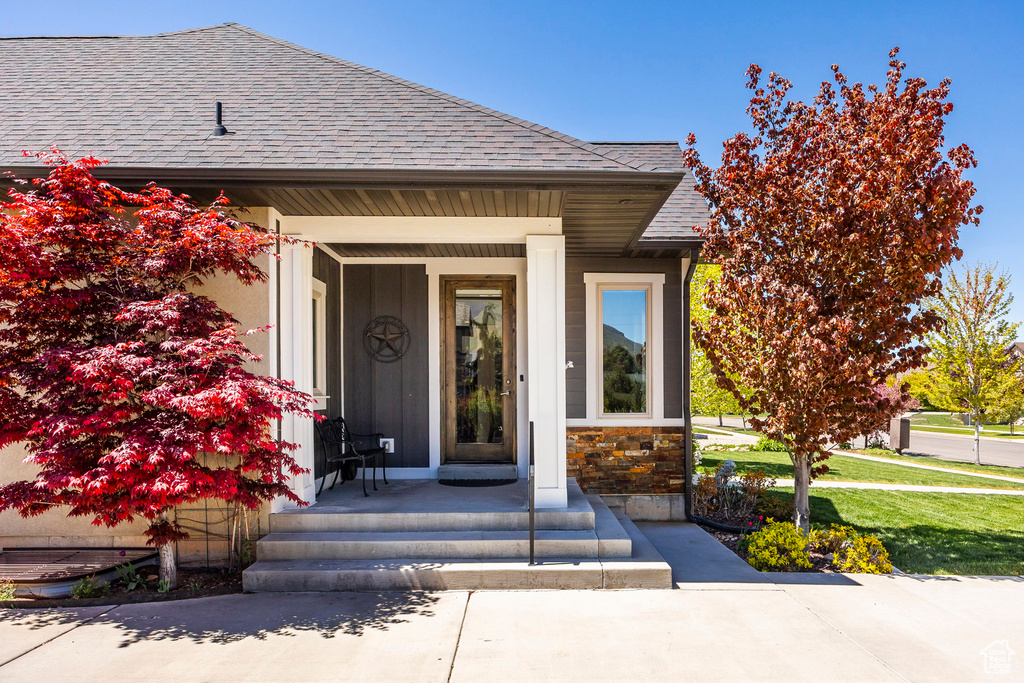 Entrance to property with stone siding, roof with shingles, and covered porch