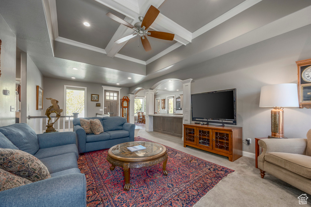 Living area with a ceiling fan, beam ceiling, decorative columns, crown molding, and light colored carpet