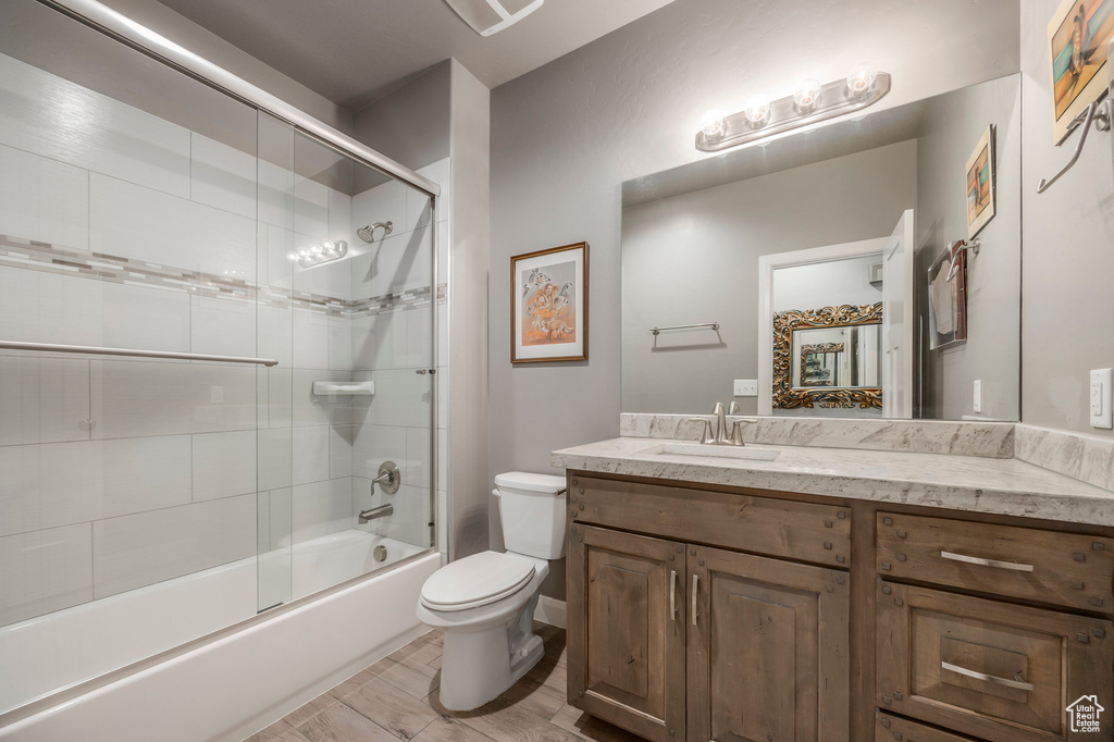 Full bath with toilet, vanity, and shower / bath combination with glass door