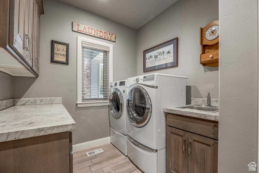 Clothes washing area with a sink, cabinet space, independent washer and dryer, visible vents, and baseboards