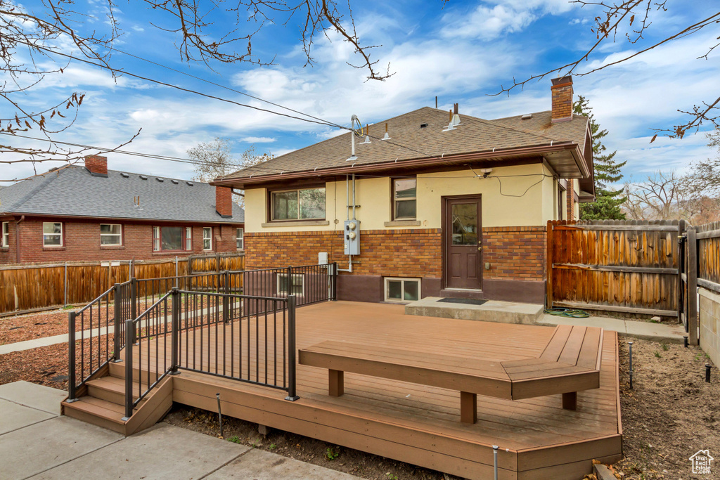 Rear view of property with a chimney, brick siding, a shingled roof, a wooden deck, and a fenced backyard