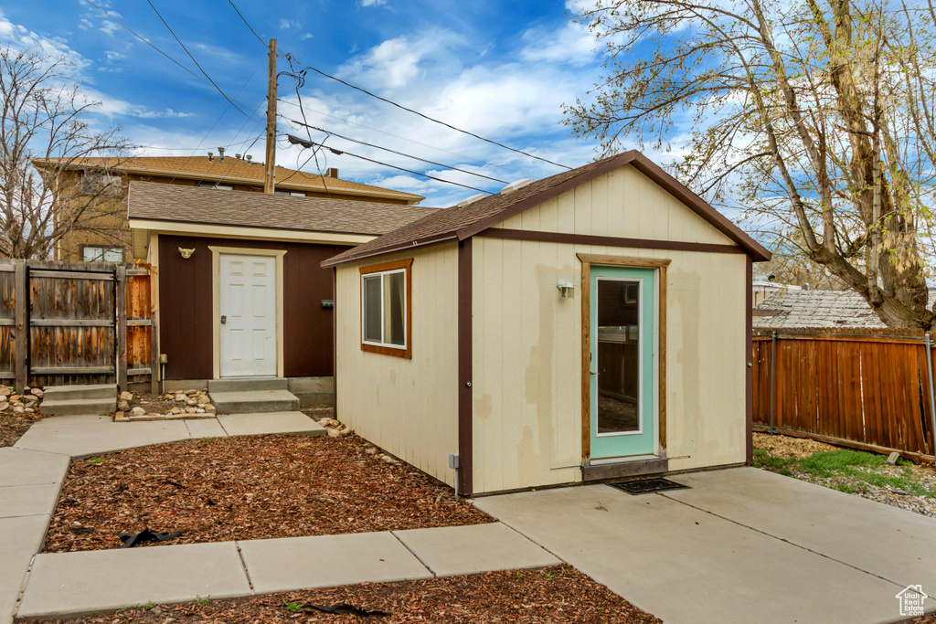 View of front facade featuring an outbuilding, roof with shingles, fence, and a patio
