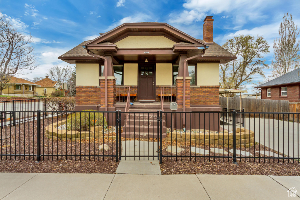 Bungalow-style home with brick siding, a porch, a chimney, and stucco siding