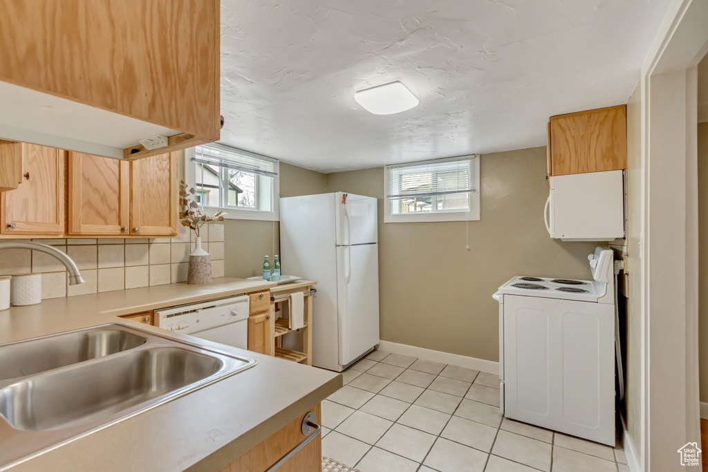 Kitchen featuring a sink, white appliances, decorative backsplash, light countertops, and light tile patterned floors