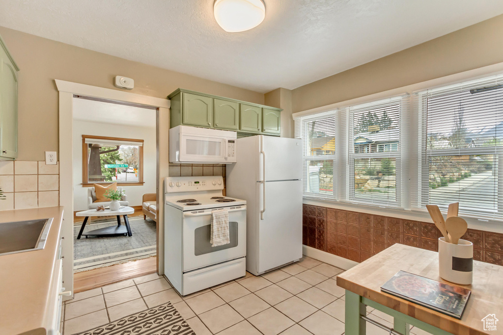 Kitchen with white appliances, green cabinetry, light tile patterned flooring, backsplash, and light countertops