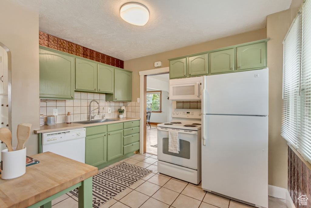Kitchen with backsplash, green cabinetry, a sink, and white appliances
