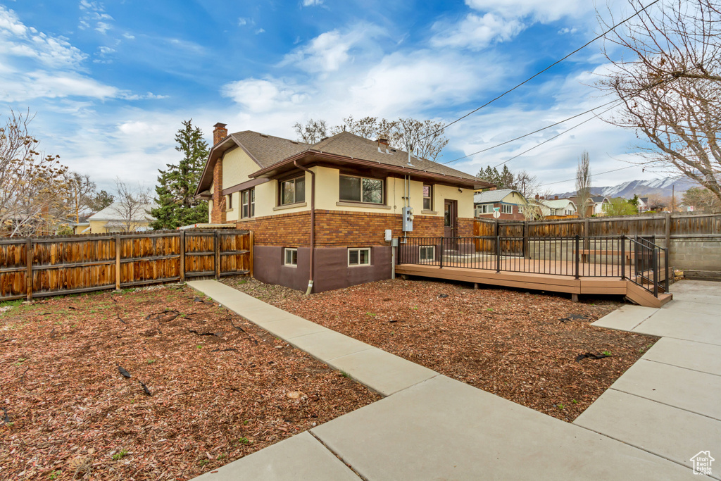 View of home's exterior featuring a chimney, a deck, brick siding, and a fenced backyard