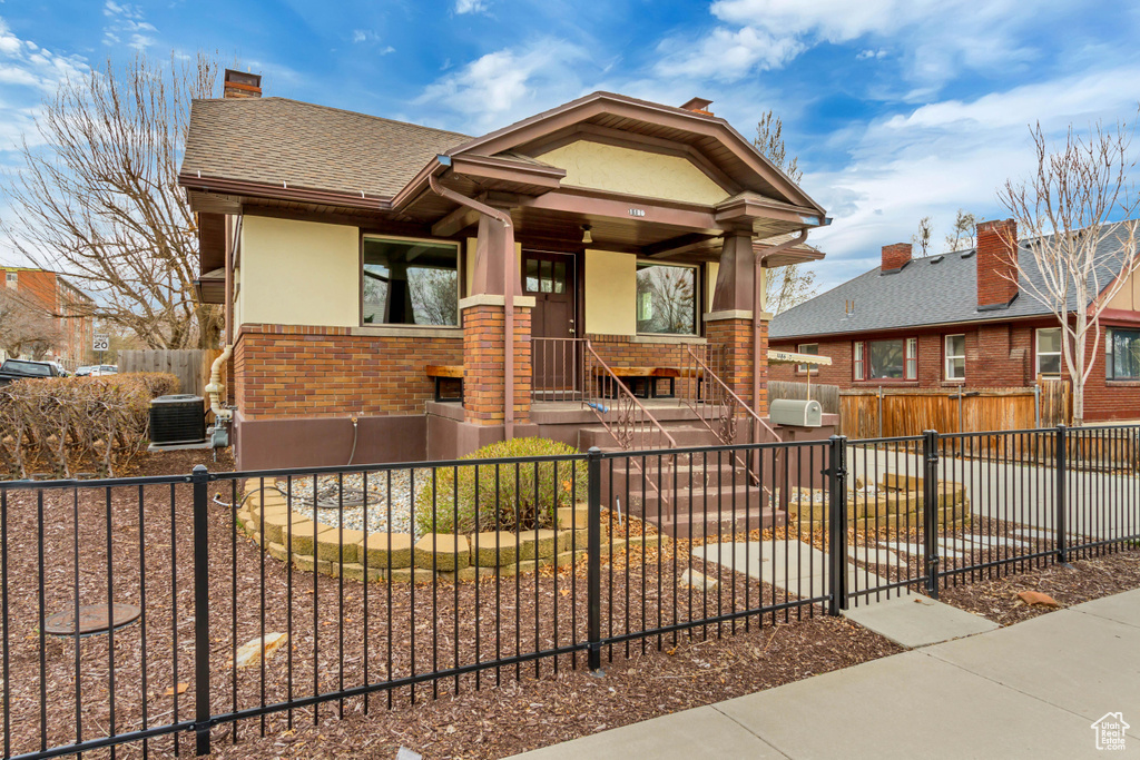 Bungalow-style house featuring brick siding, stucco siding, a fenced front yard, a chimney, and a shingled roof