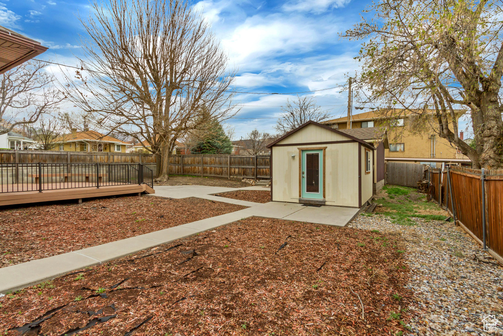 View of yard featuring a storage unit, a deck, a fenced backyard, an outbuilding, and a patio area