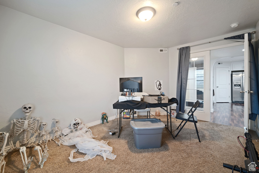 Carpeted office with a textured ceiling and baseboards