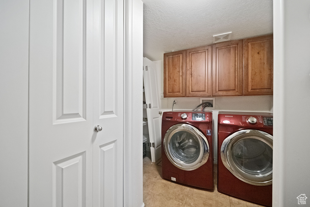 Clothes washing area with light tile patterned floors, cabinet space, washer and clothes dryer, visible vents, and a textured ceiling