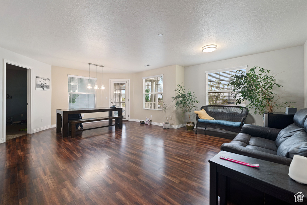 Living area featuring baseboards, a textured ceiling, a notable chandelier, and dark wood-style floors