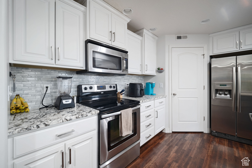 Kitchen with light stone counters, visible vents, white cabinets, appliances with stainless steel finishes, and dark wood-style floors