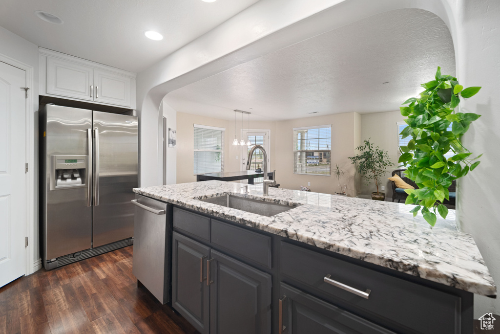 Kitchen featuring a sink, stainless steel appliances, dark wood finished floors, white cabinetry, and light stone countertops