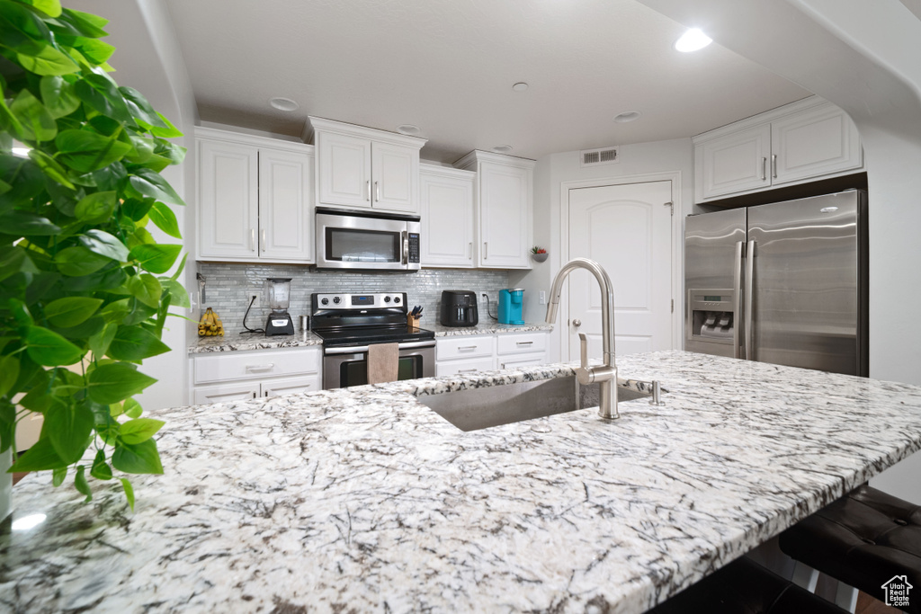 Kitchen with light stone counters, visible vents, a sink, a kitchen breakfast bar, and stainless steel appliances