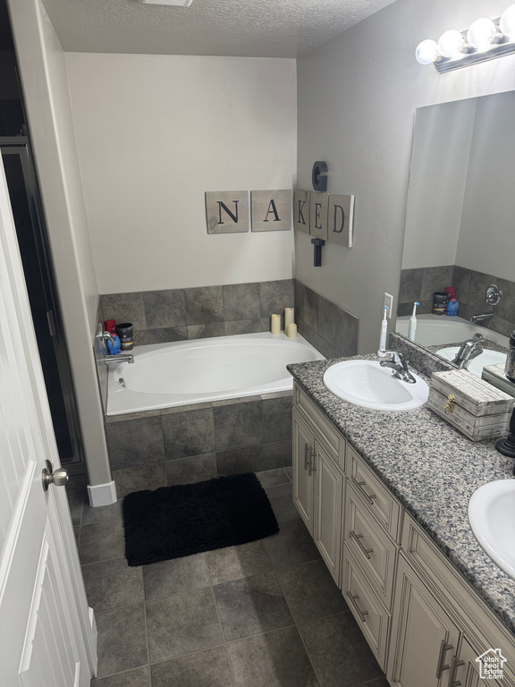 Full bathroom featuring a sink, double vanity, a textured ceiling, and a garden tub