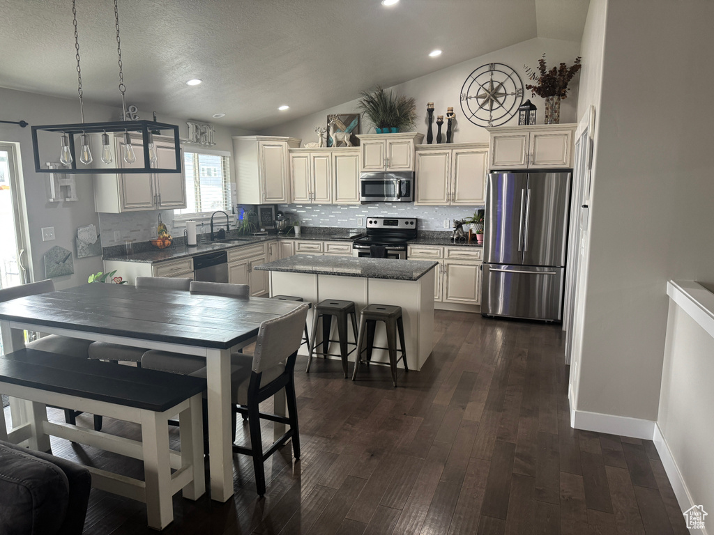 Kitchen featuring a kitchen island, lofted ceiling, decorative backsplash, and appliances with stainless steel finishes