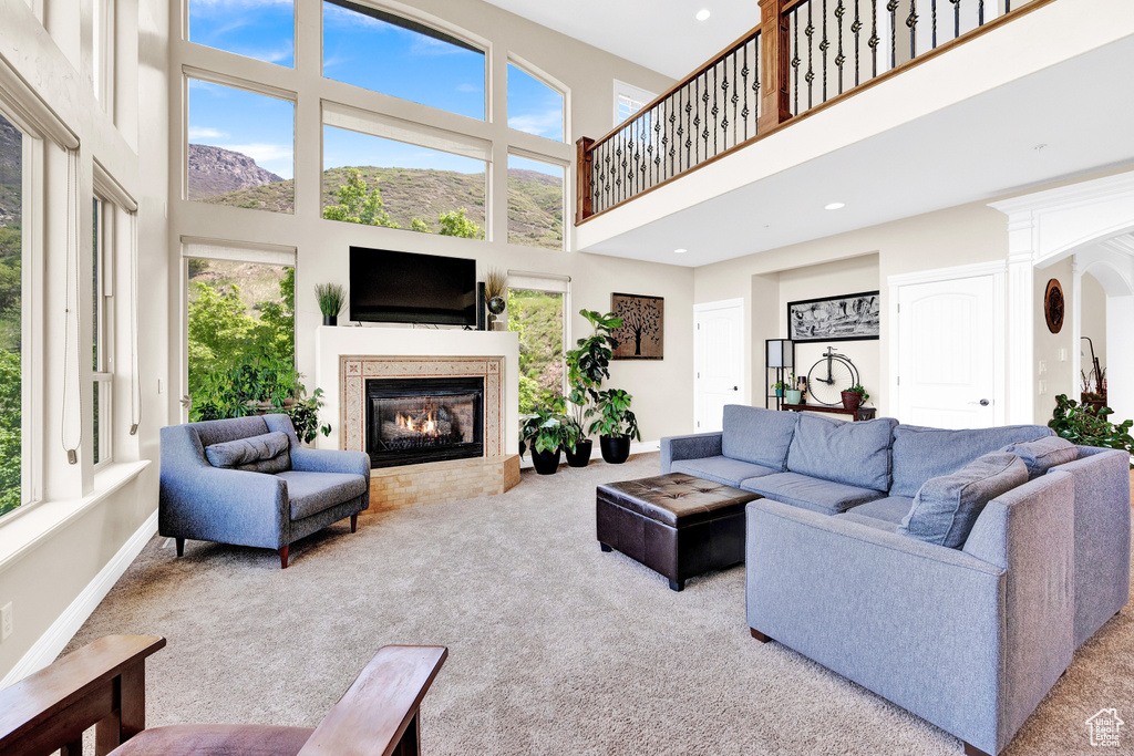 Carpeted living area featuring baseboards, a glass covered fireplace, recessed lighting, and a towering ceiling