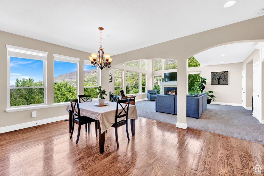 Dining area with wood finished floors, an inviting chandelier, arched walkways, baseboards, and a glass covered fireplace