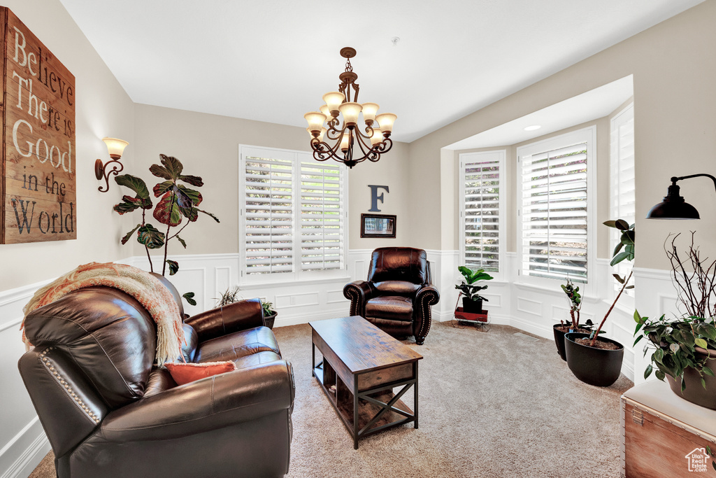 Carpeted living room featuring an inviting chandelier, a decorative wall, and a wainscoted wall