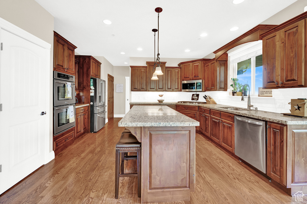Kitchen featuring light wood finished floors, a sink, a kitchen island, backsplash, and stainless steel appliances