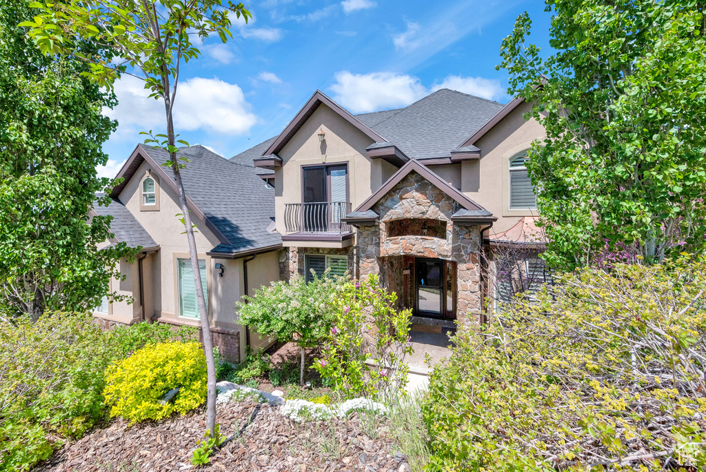 Craftsman house with roof with shingles, stucco siding, stone siding, and a balcony
