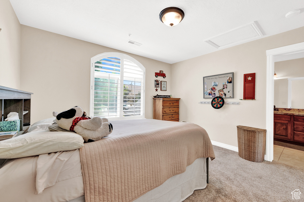 Bedroom featuring ensuite bathroom, attic access, visible vents, light carpet, and baseboards