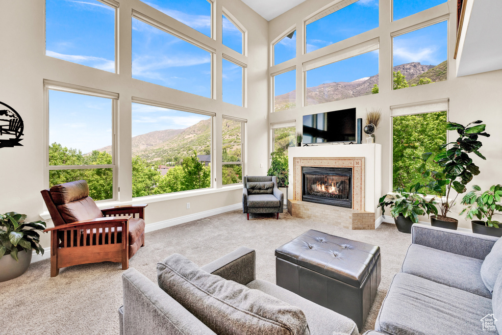 Carpeted living area featuring baseboards, a towering ceiling, and a glass covered fireplace