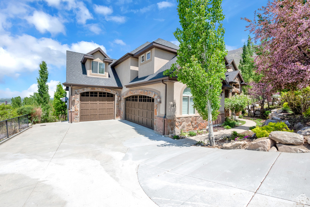 Craftsman-style house featuring driveway, fence, stucco siding, stone siding, and roof with shingles