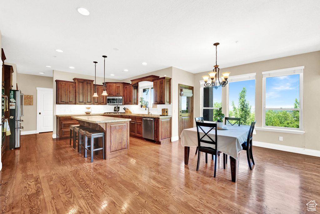 Kitchen with stainless steel appliances, wood finished floors, a breakfast bar, a chandelier, and a center island