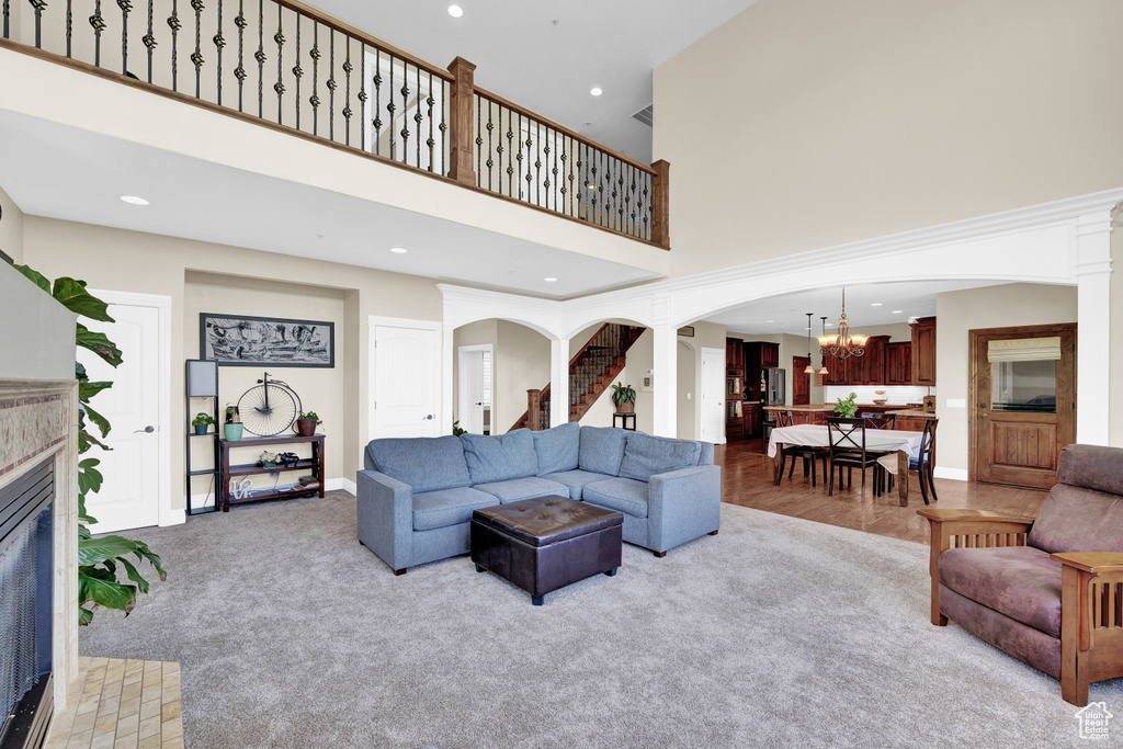 Living room with a high ceiling, an inviting chandelier, a tiled fireplace, arched walkways, and light colored carpet