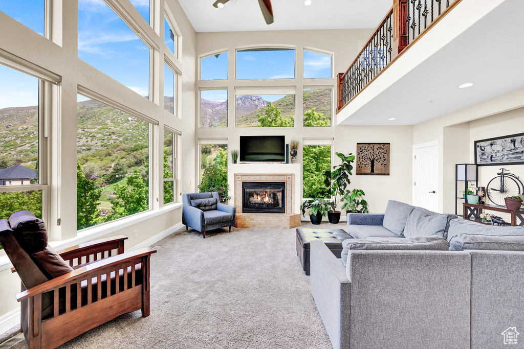Carpeted living area with recessed lighting, ceiling fan, a high ceiling, baseboards, and a glass covered fireplace