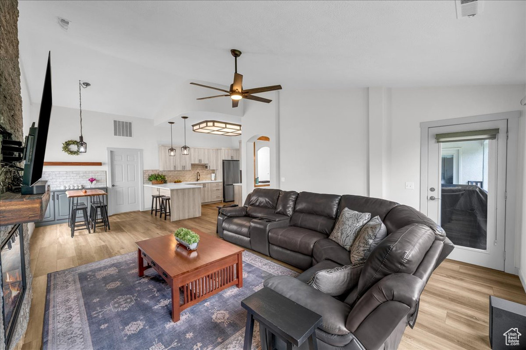 Living room with visible vents, ceiling fan, arched walkways, light wood-style floors, and lofted ceiling
