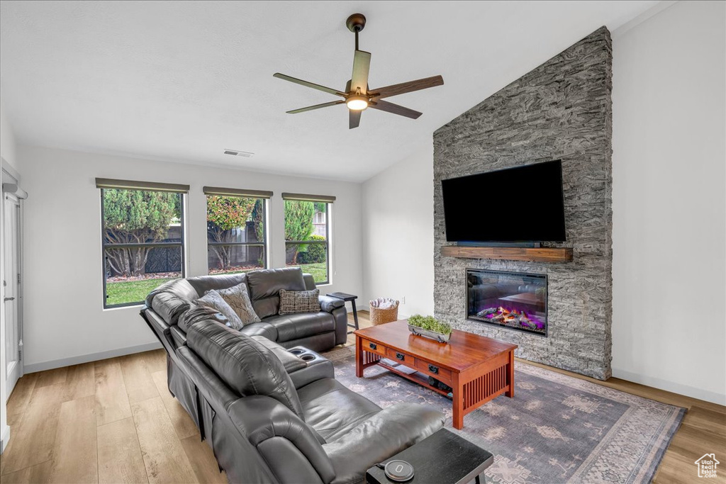 Living room featuring wood finished floors, a ceiling fan, visible vents, a stone fireplace, and vaulted ceiling