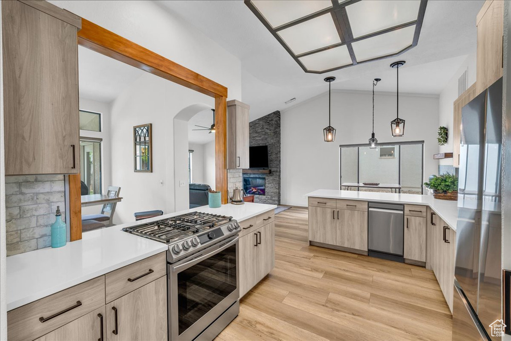 Kitchen with a peninsula, light brown cabinetry, a fireplace, light countertops, and appliances with stainless steel finishes