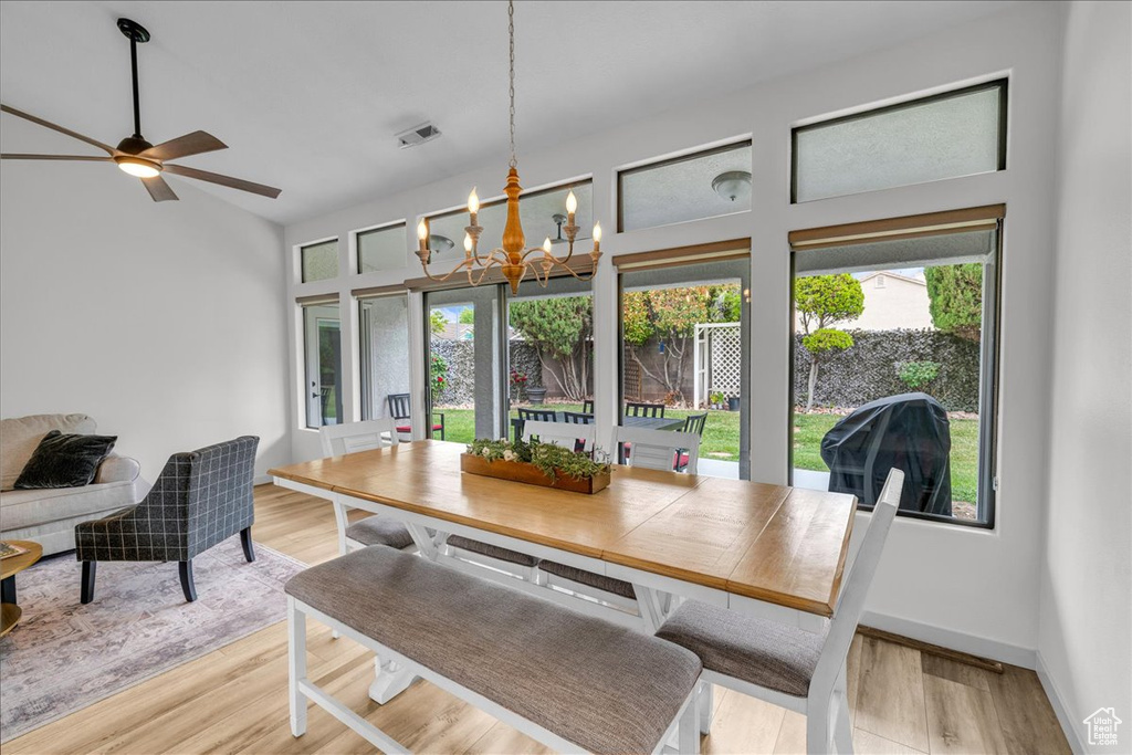 Dining space with ceiling fan with notable chandelier, plenty of natural light, and light wood-style floors