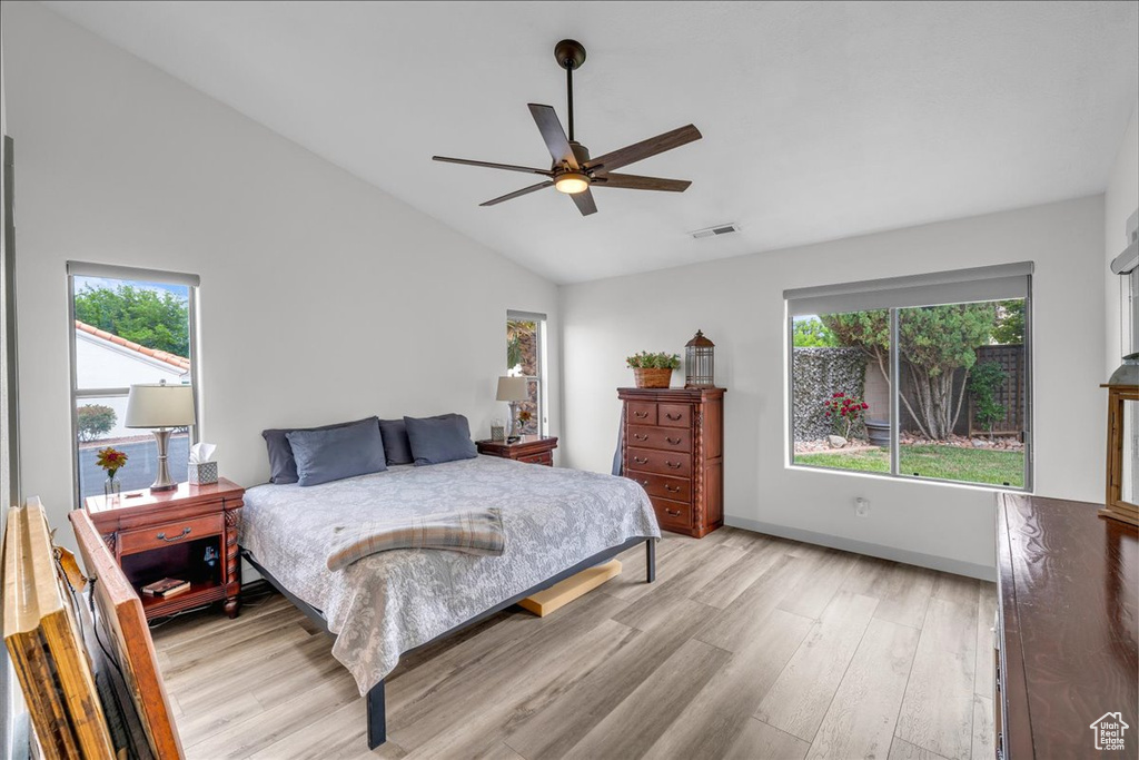 Bedroom featuring vaulted ceiling, multiple windows, visible vents, and light wood-style floors