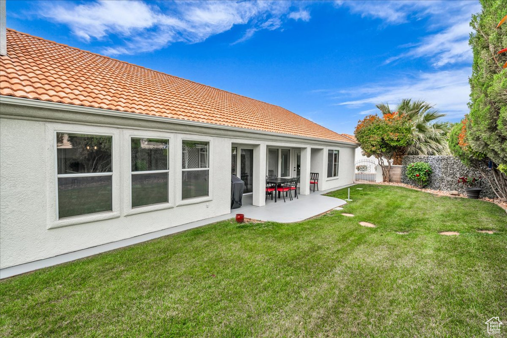 Back of property with stucco siding, a tile roof, fence, a yard, and a patio area