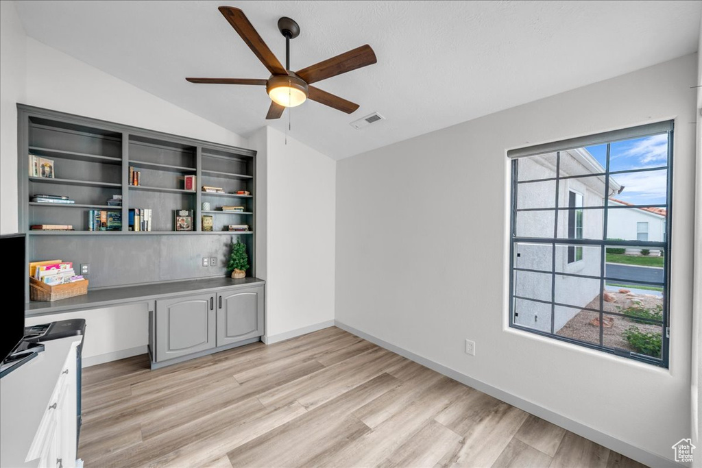 Interior space featuring built in desk, light wood-style flooring, lofted ceiling, and ceiling fan