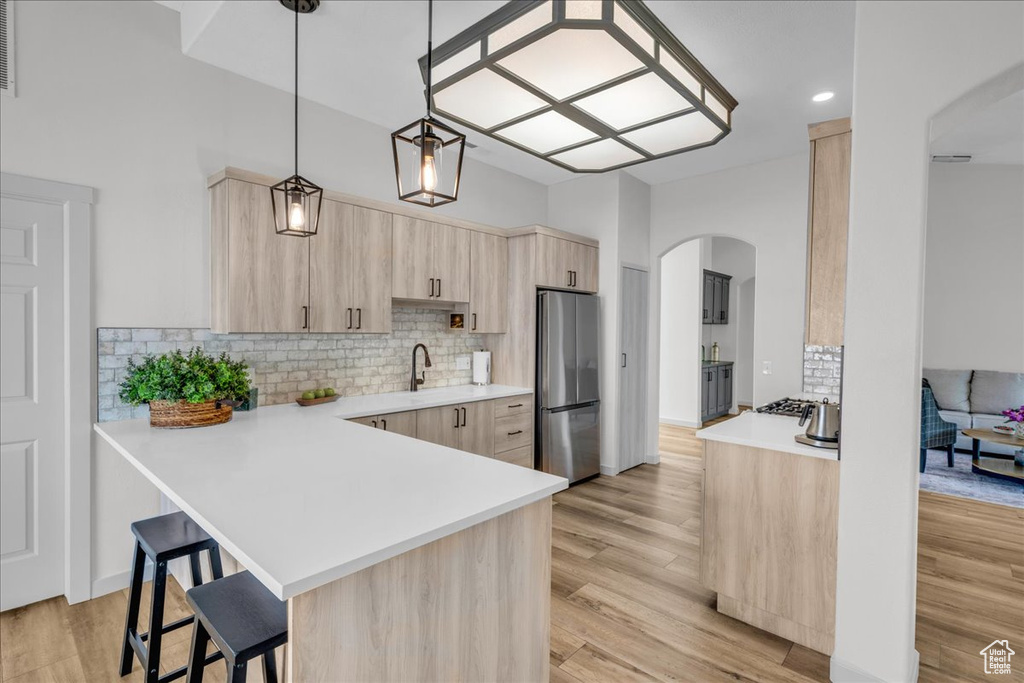 Kitchen with light brown cabinets, a peninsula, a kitchen breakfast bar, arched walkways, and stainless steel appliances