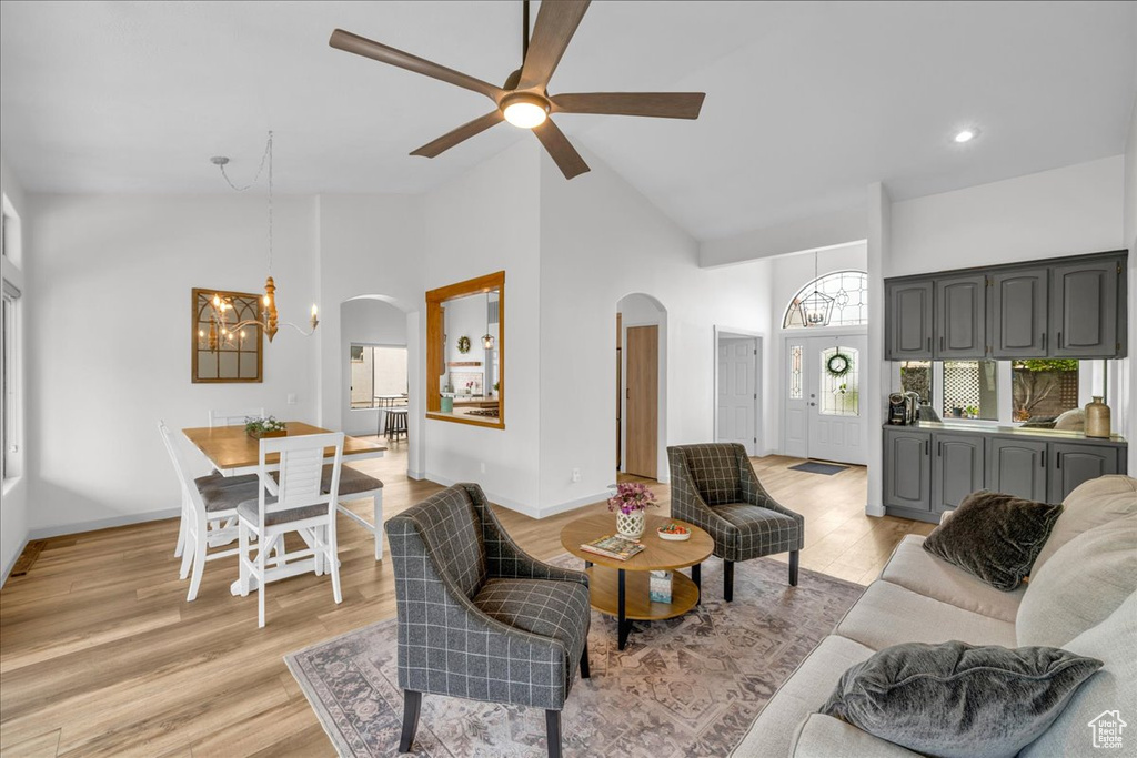 Living room with light wood-style flooring, ceiling fan with notable chandelier, arched walkways, and high vaulted ceiling