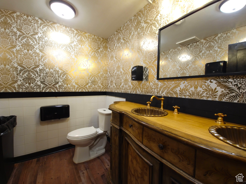 Half bath with wainscoting, wallpapered walls, and wood finished floors