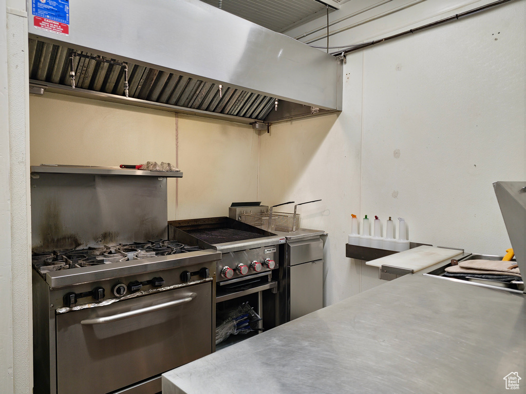 Kitchen with stainless steel counters, range hood, fridge, and stainless steel range with gas cooktop
