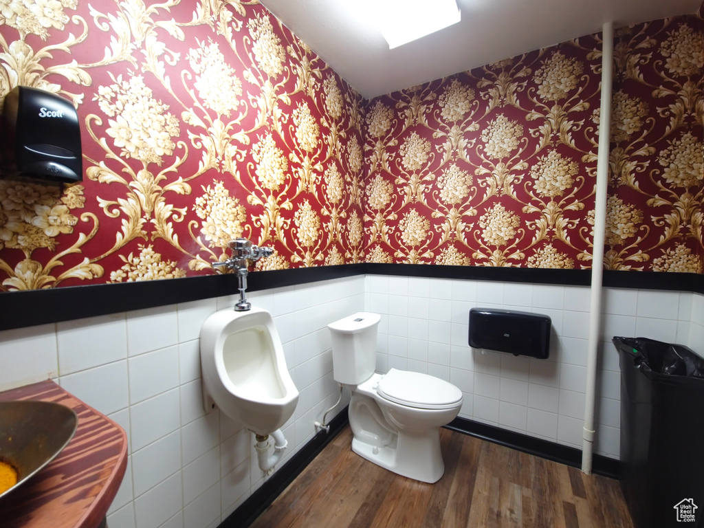 Bathroom featuring toilet, tile walls, wood finished floors, wainscoting, and wallpapered walls